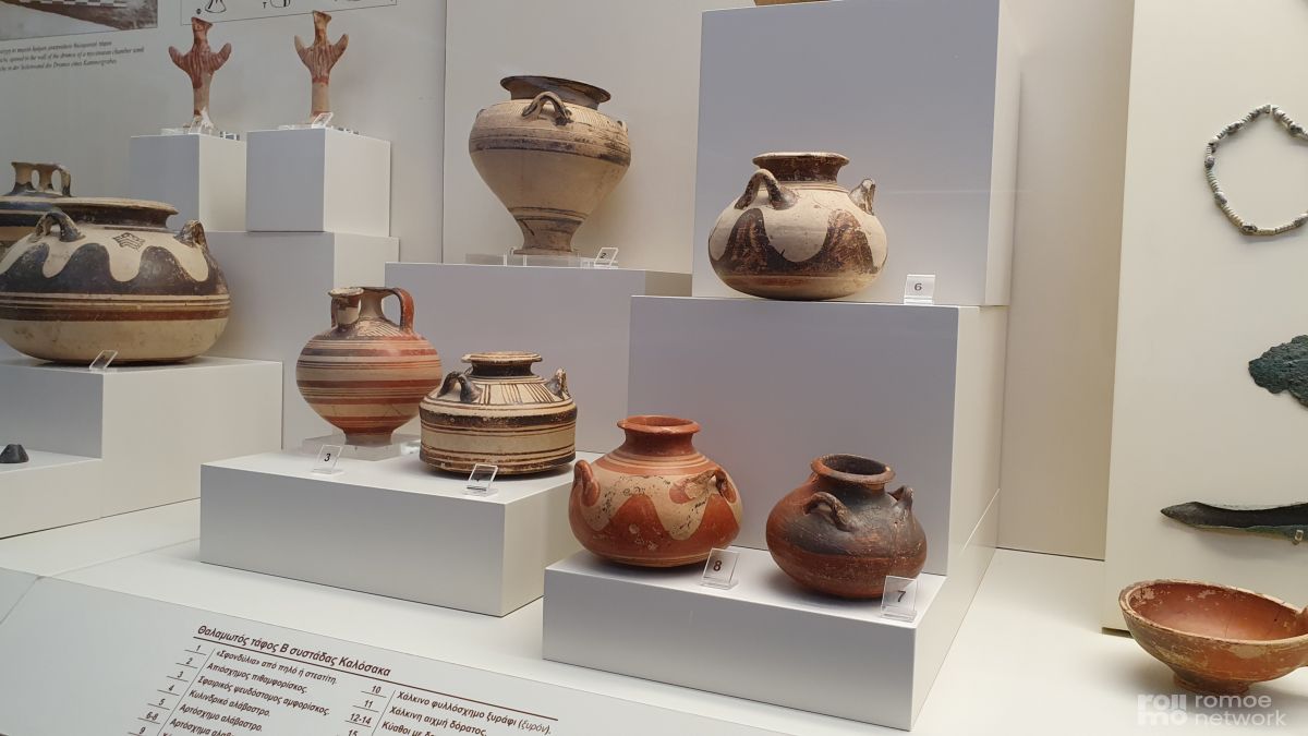 Antike griechische Keramiken mit geometrischen Mustern und Erdfarben, ausgestellt auf weißen Sockeln im Museum.