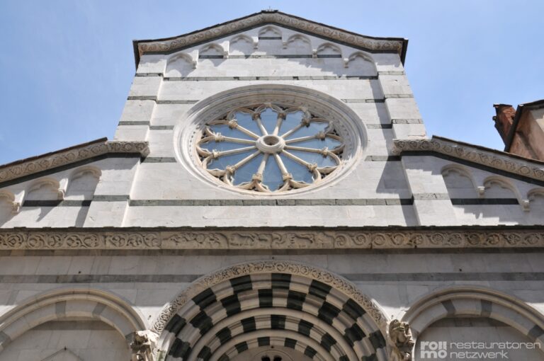 Die Fassade zeigt eine Steinkirche mit Streifen, großem Rundfenster und verzierten Bögen über dem Eingang.