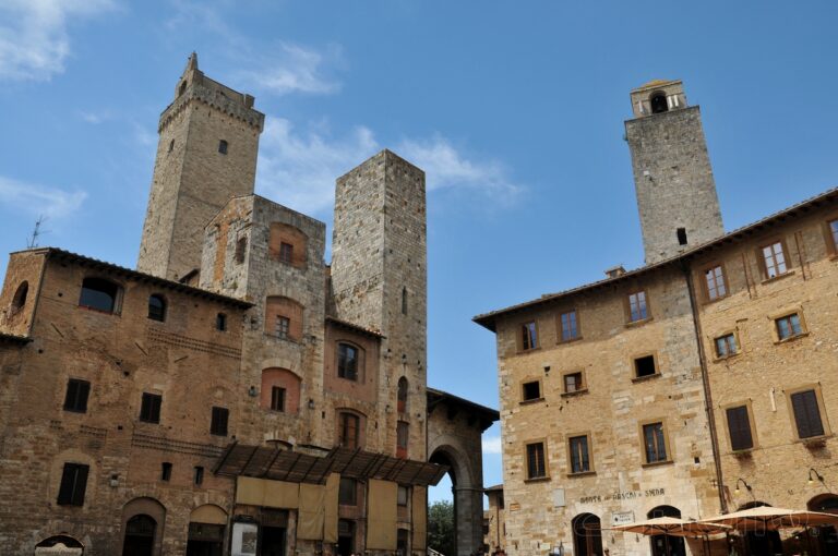 Mittelalterliche Steintürme und Gebäude mit Rundbogenfenstern auf einem Platz in San Gimignano, Italien, bei klarem Himmel.